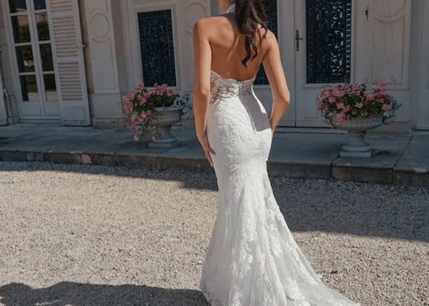Bride wearing a fitted lace halter neckline wedding dress with open back and train, standing outdoors in front of a classic building.