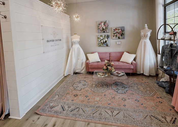Elegant bridal boutique reception area with a pink sofa, wedding gowns on display, floral wall art, and Olivier Couture signage.