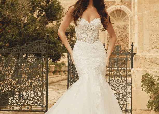 Bride in a lace mermaid wedding dress with a sweetheart neckline standing outdoors by a wrought iron gate