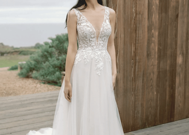 Bride in a deep V-neck wedding dress with lace bodice and soft tulle skirt standing near a wooden wall.
