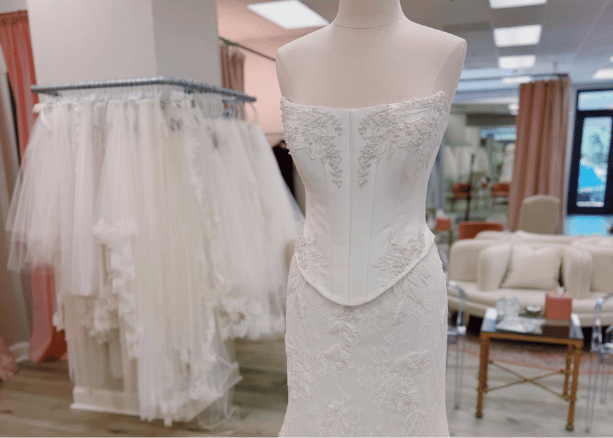 Strapless lace wedding dress on a mannequin surrounded by bridal fabrics and gowns