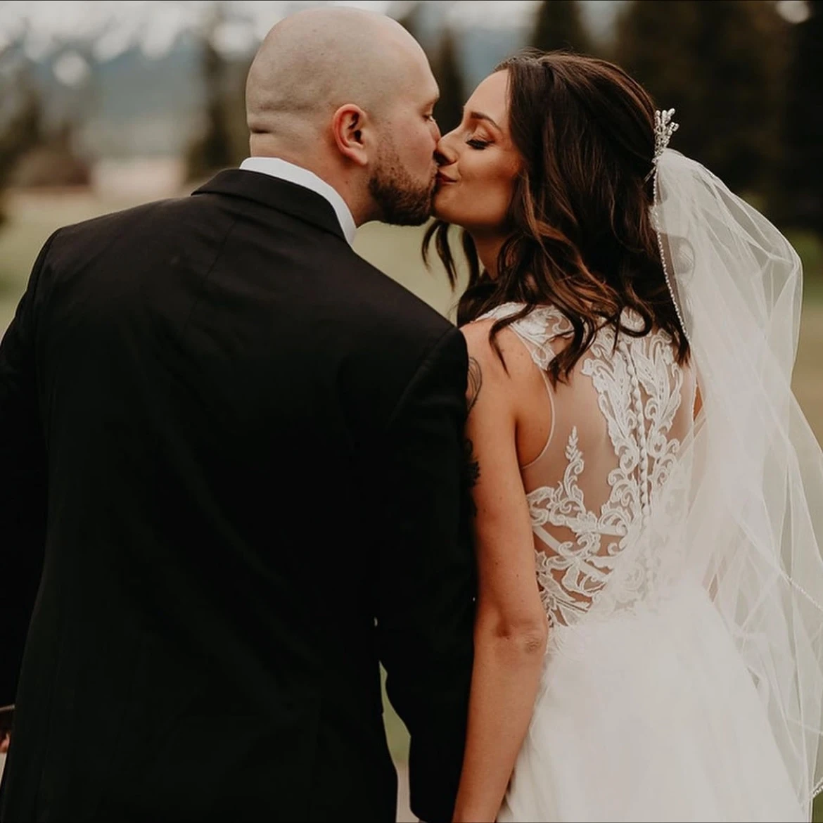 Close-up of a bride and groom, highlighting the bride's wedding gown with a detailed lace back design.