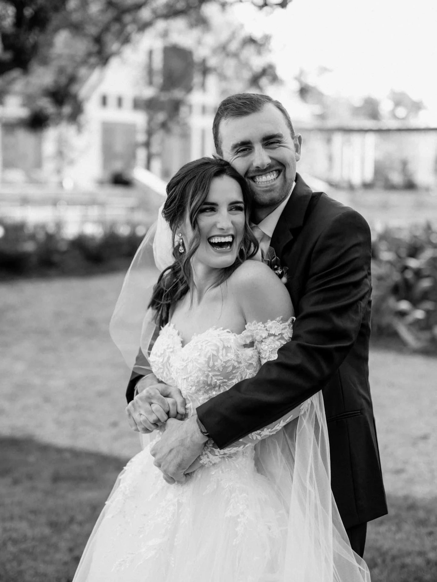 Happy bride and groom smiling, showcasing the bride’s off-shoulder wedding gown with floral detailing.