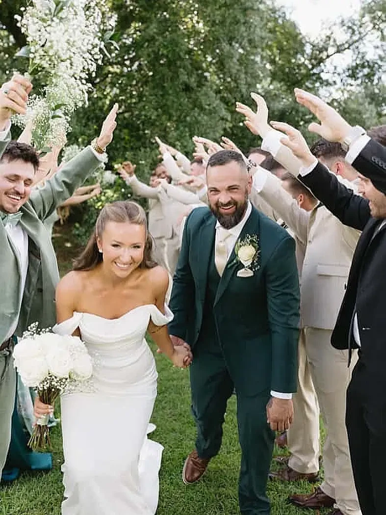 Bride and groom smiling while walking through a celebratory arch of guests outdoors